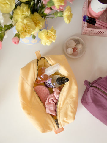 A yellow quilted makeup bag on a table, open to reveal beauty products.