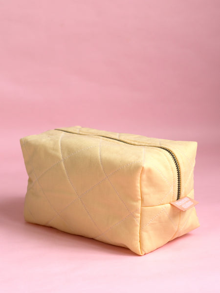 A yellow quilted makeup bag on a pink foreground.