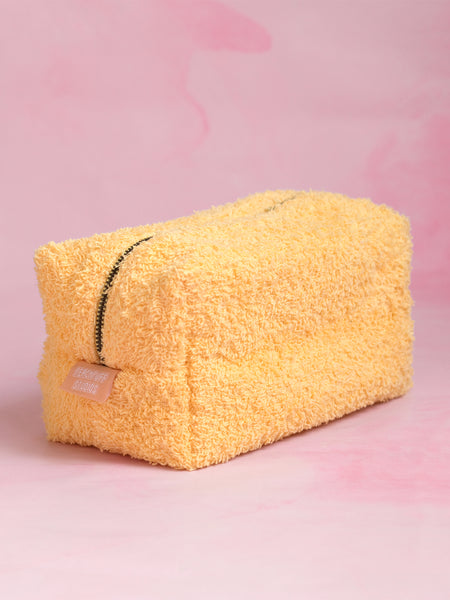 A yellow towelling makeup bag on a pink marbled foreground.