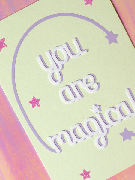 Art print with You Are Magical in flocked font with a purple curved line with a star at the end, coming off with M and L of magical. 