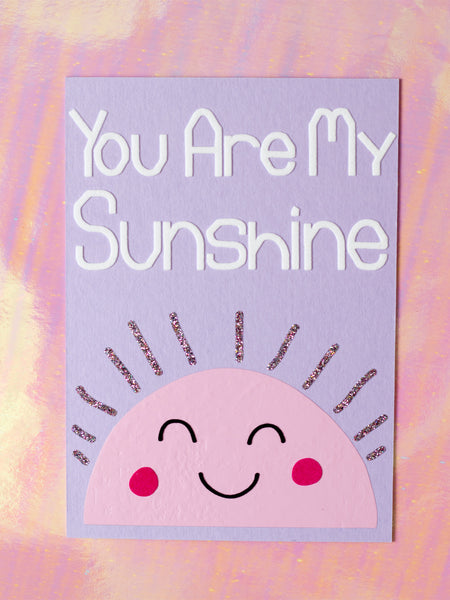 Art print with You Are My Sunshine in flocked font on top of a pink, simple drawn sun, with glittery beams and a cute face.
